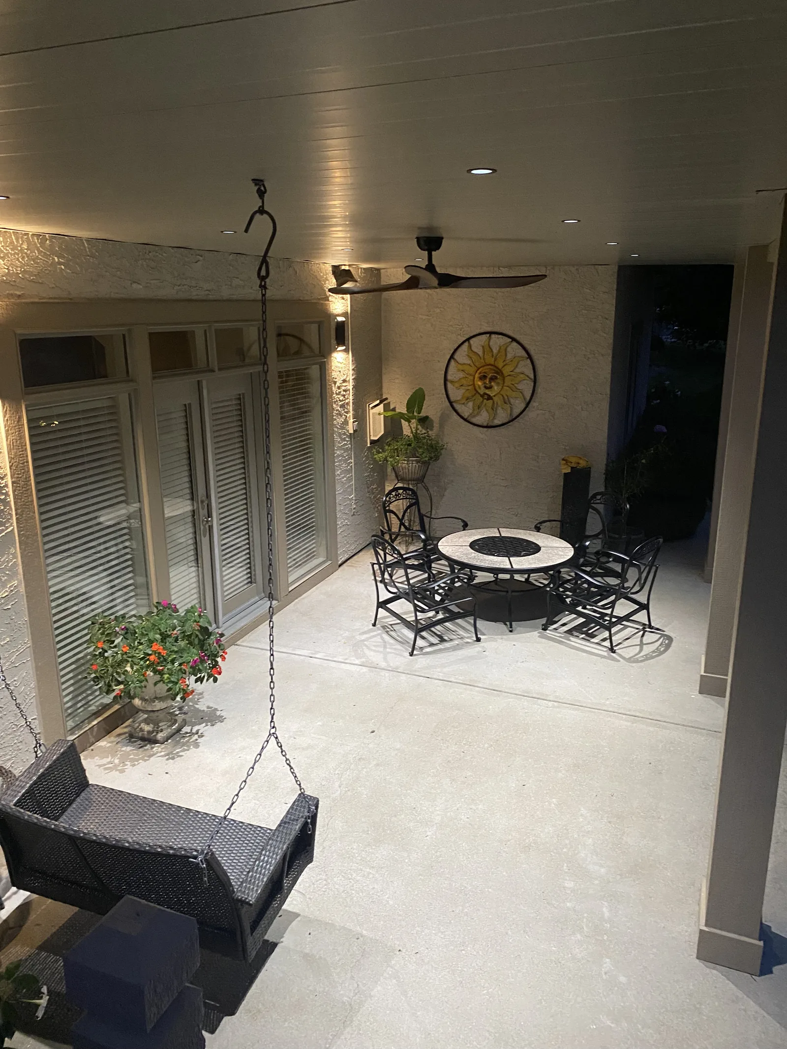 A finished under-deck ceiling at dusk with recessed lights and a ceiling fan over a stone patio dining set